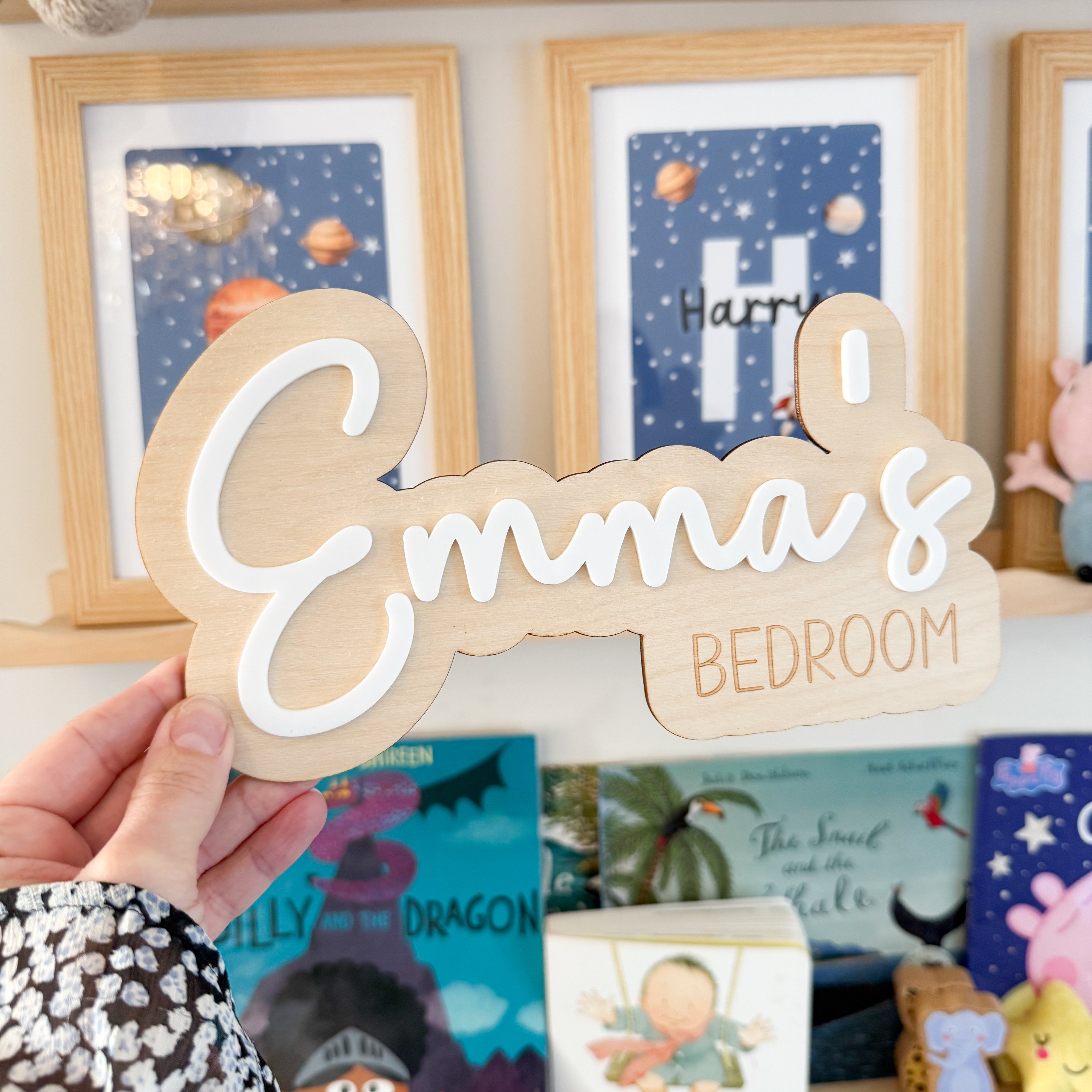 A hand is holding a wooden sign with the name "Emma&