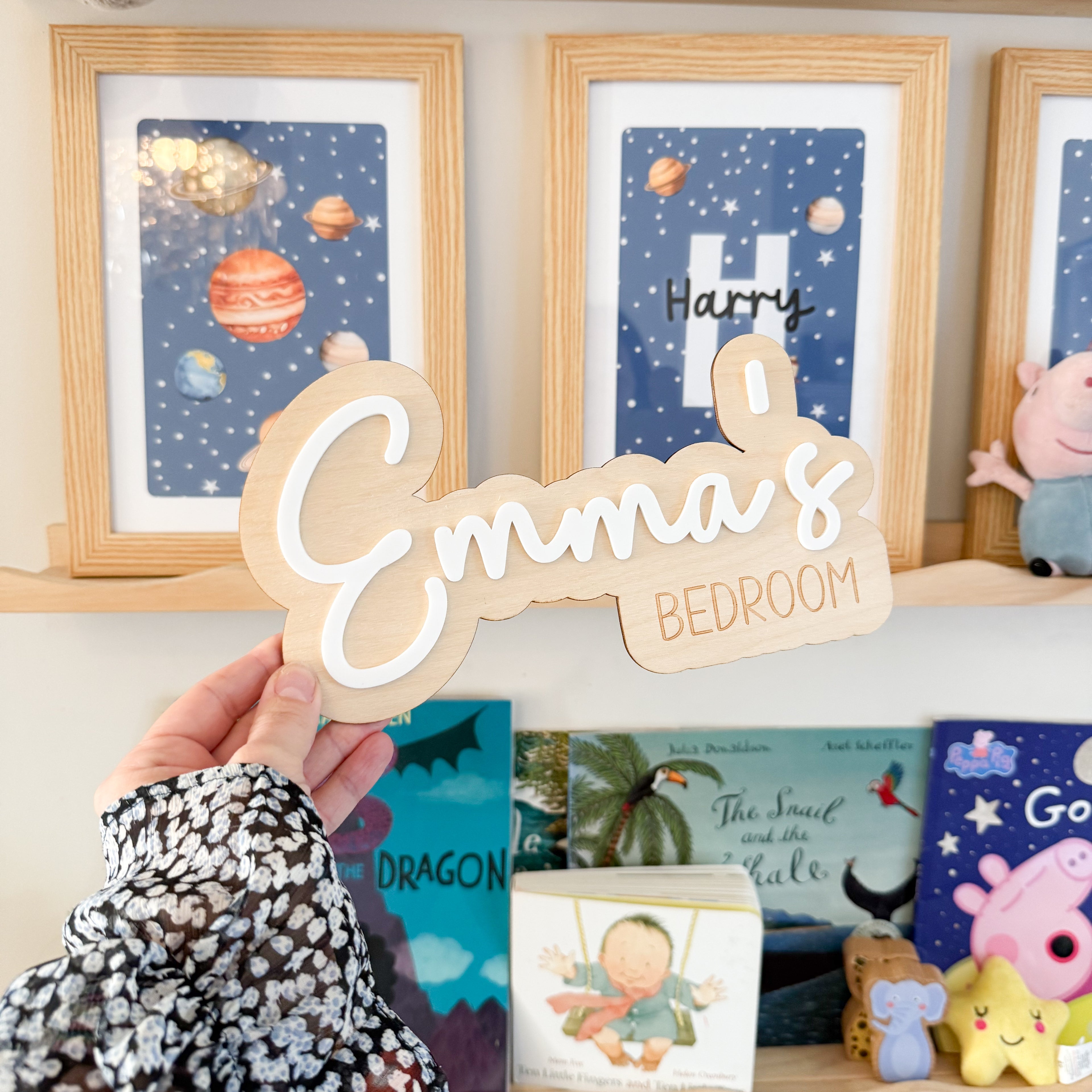 A hand holding a wooden sign with the name "Emma&
