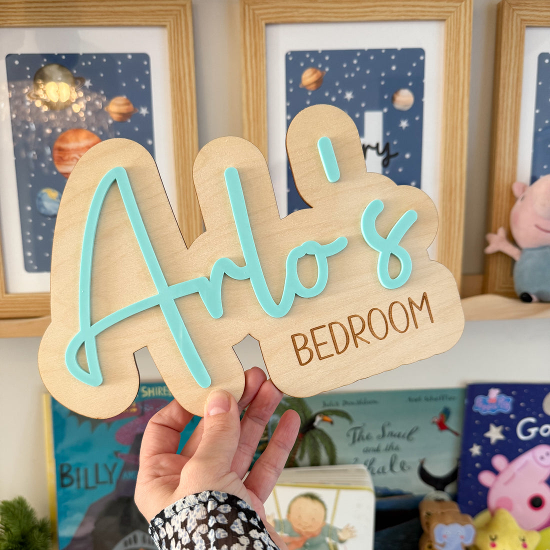 A hand is holding a wooden sign with the name &quot;Arlo&